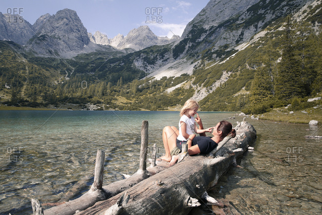 Austria- Tyrol- playful mother and daughter on tree trunk at lake Seebensee