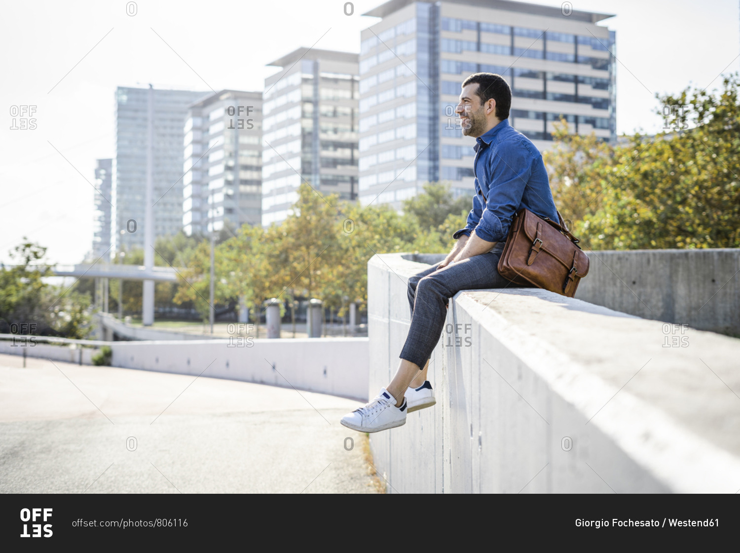 Relaxed man with leather bag sitting on wall