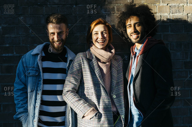 Portrait of three happy friends in shadow at a brick wall
