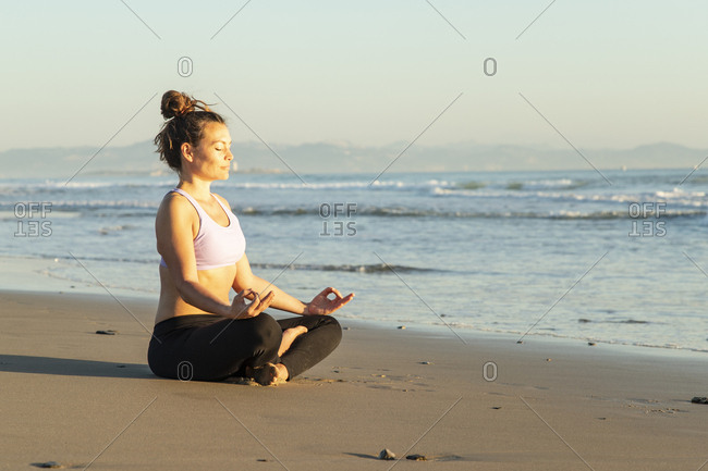 Woman meditating on the beach in the evening