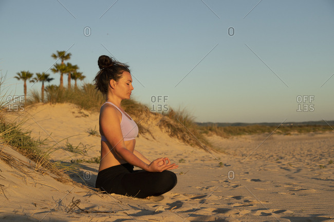 Woman meditating on the beach in the evening