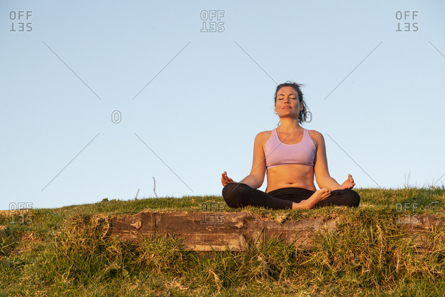 Woman meditating on a meadow in the evening