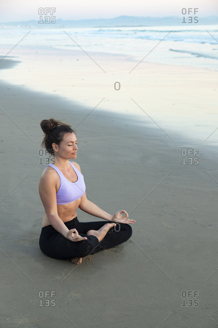 Woman meditating on the beach in the evening