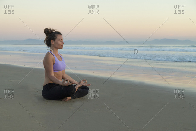 Woman meditating on the beach in the evening