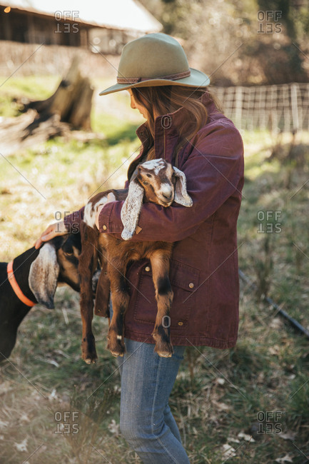 Woman holding a baby goat petting a mama goat.