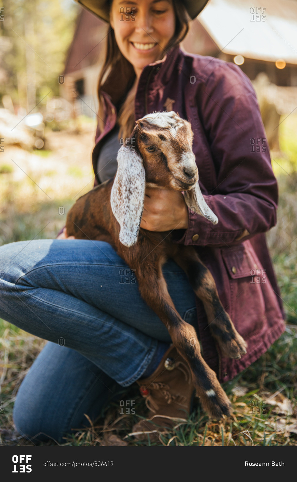 Smiling woman sitting down holding a baby goat.