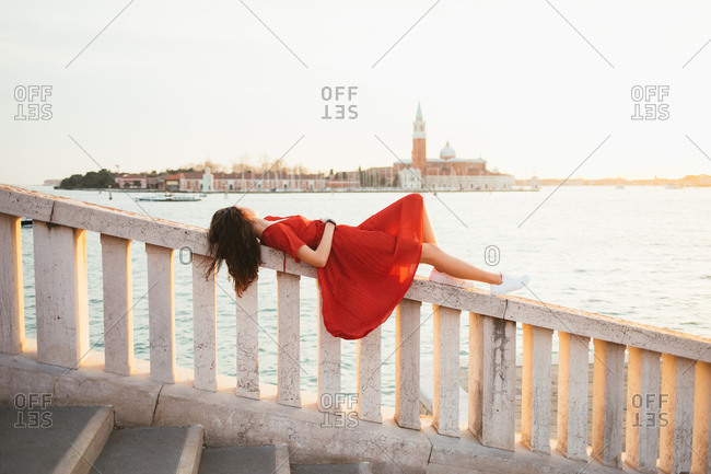 Woman in red dress, laying down looking at the sunset, in Venice