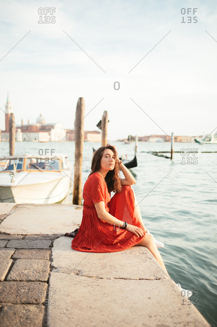 Woman in red dress sitting near a Venice channel