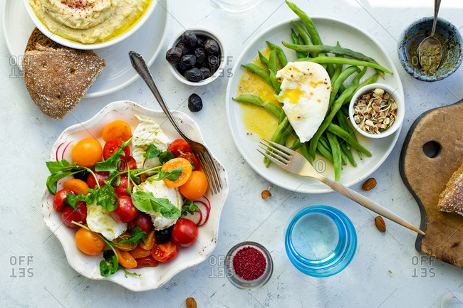 Overhead image of healthy lunch with mozarella tomato salad, green beans with poached egg and hummus
