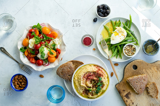 Overhead image of healthy lunch with mozarella tomato salad, green beans with poached egg and hummus