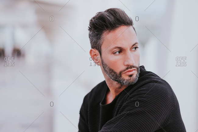 Adult handsome elegant cheerful male in casual wear looking away on city street