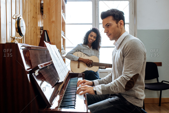 Side view of young man playing piano near black woman playing guitar in music studio