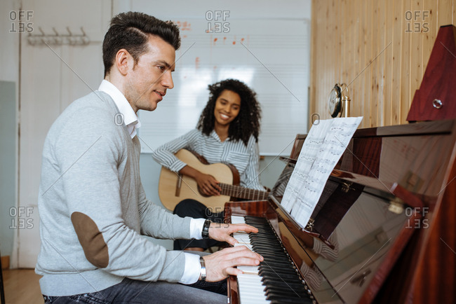 Side view of young man playing piano near black woman playing guitar in music studio
