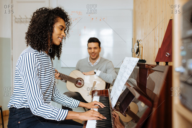 Side view of young black woman playing piano near man playing guitar in music studio