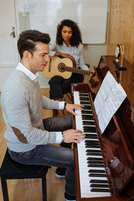 Side view of young man playing piano near black woman playing guitar in music studio