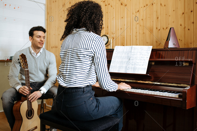 Back view of young black woman playing piano near man playing guitar in music studio