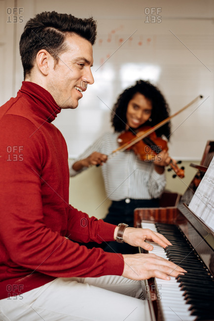 Side view of young man playing piano near black woman playing violin in music studio