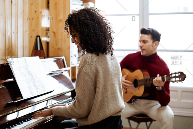 Side view of young black woman playing piano near man playing guitar in music studio