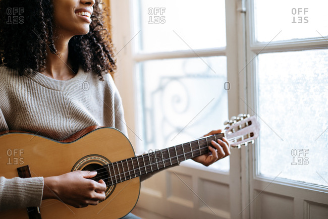Black woman playing guitar during rehearsal in recording studio.