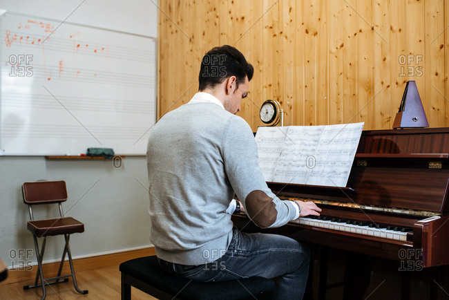 Back view of a handsome man playing piano during rehearsal in recording studio.