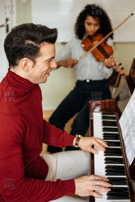 Side view of young man playing piano near black woman playing violin in music studio