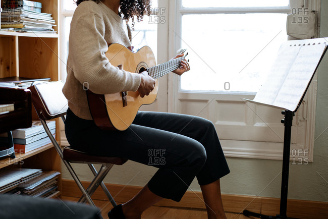 Black woman playing guitar during rehearsal in recording studio.