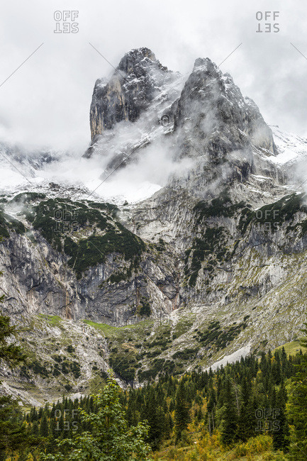 Rugged mountain peak and valley with peak coming through cloud covering and snow; Grainau, Bavaria, Germany
