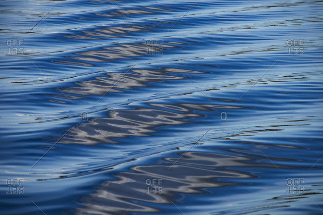 The blue, black, and white reflections of the sky, clouds, and nearby land on the wake of a boat in the Puget Sound, Washington, creating a lovely texture and sense of movement; Puget Sound, Washington, United States of America