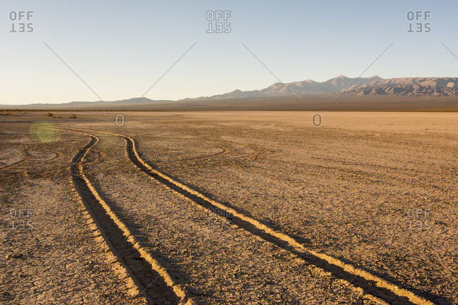 Tire tracks through a dry lake bed lead the eye to wards a mountain range at dawn; Barreal, San Juan, Argentina