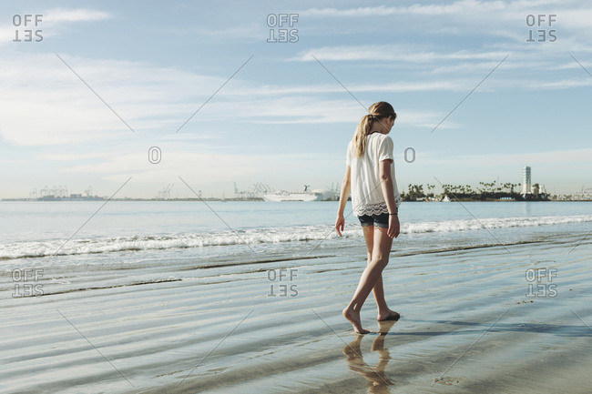 A girl walking on the beach on the wet sand; Long Beach, California, United States of America
