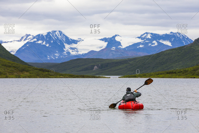 A man paddles a packraft across Landmark Gap Lake with the Alaska Range in the distance; Alaska, United States of America