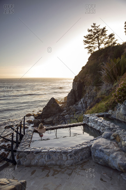 USA, California, Big Sur, Esalen,  - May 13, 2013: a woman sits in the Baths and looks out on the Big Sur coastline at sunset, the Esalen Institute