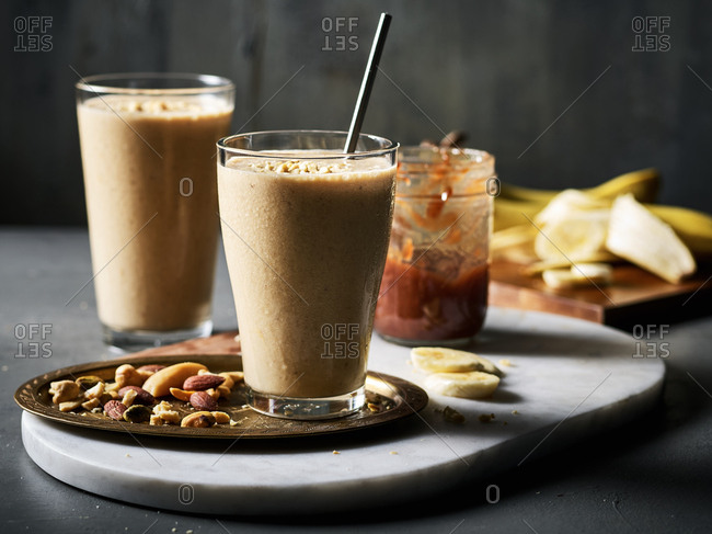 Two peanut butter, banana, and jam smoothies with jam and bananas and a tray of nuts