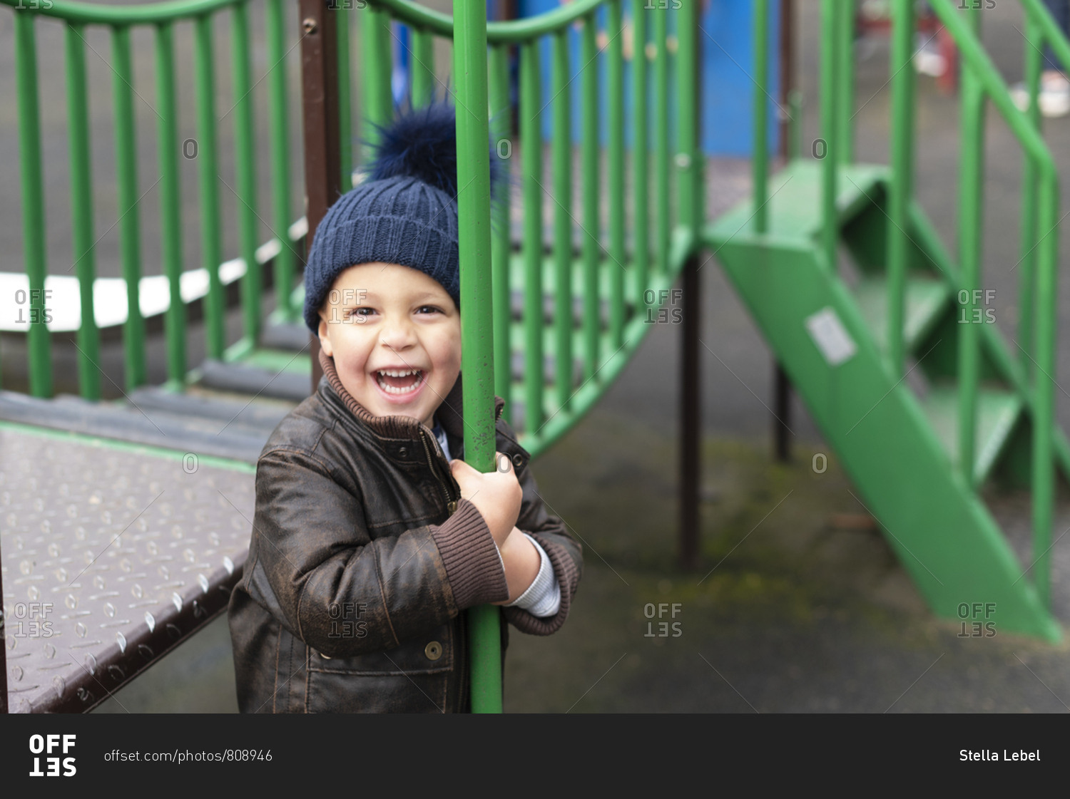Happy young boy in playground holds fireman's pole