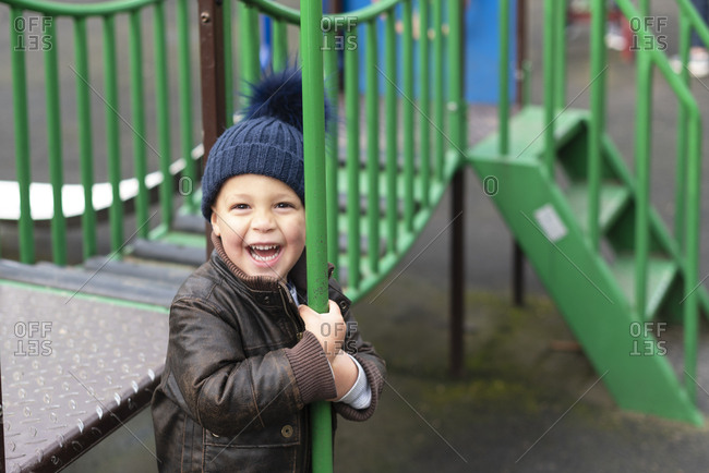 Happy young boy in playground holds fireman\'s pole