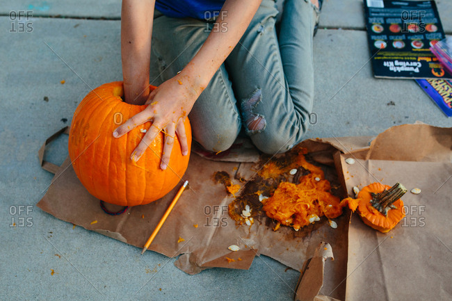 Girl reaches into pumpkin to remove insides with other hand messy