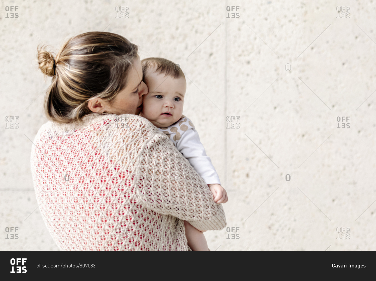 Mom holding and kissing baby who is waking up against concrete wall