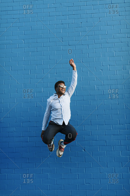 Stylish black man wearing blue striped collared shirt jumping in the air