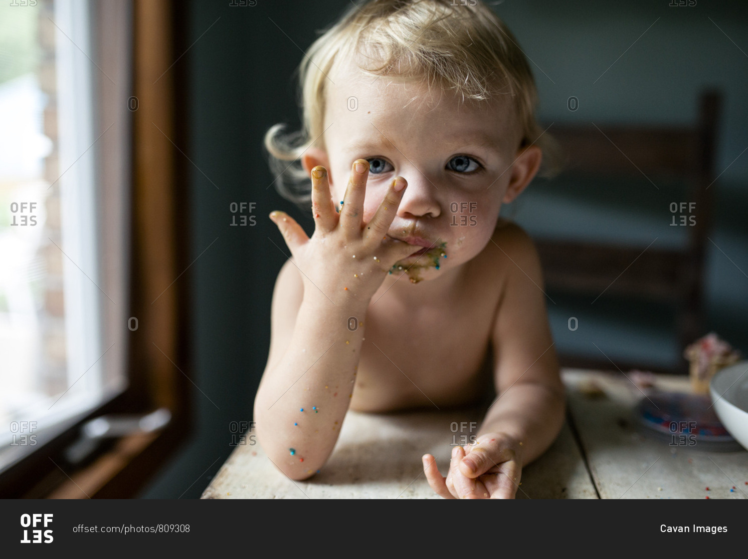 Toddler girl licking sticky fingers with colorful sprinkles stock photo OFFSET