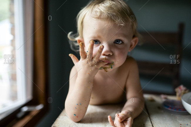 Toddler girl licking sticky fingers with colorful sprinkles