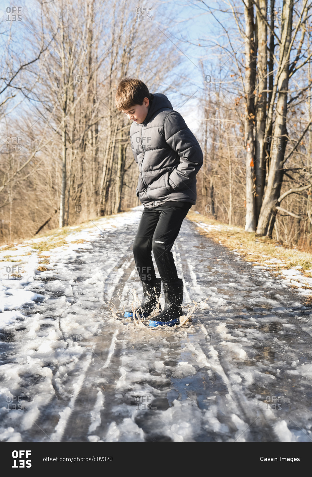 Preteen boy jumping in a slushy puddle on a hiking trail in winter.