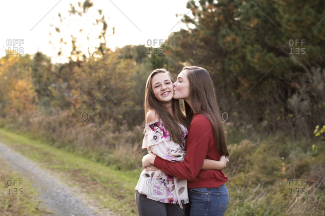 Teen Girl Kisses Teen Sister on Cheek on a Trail at Sunset in Fall