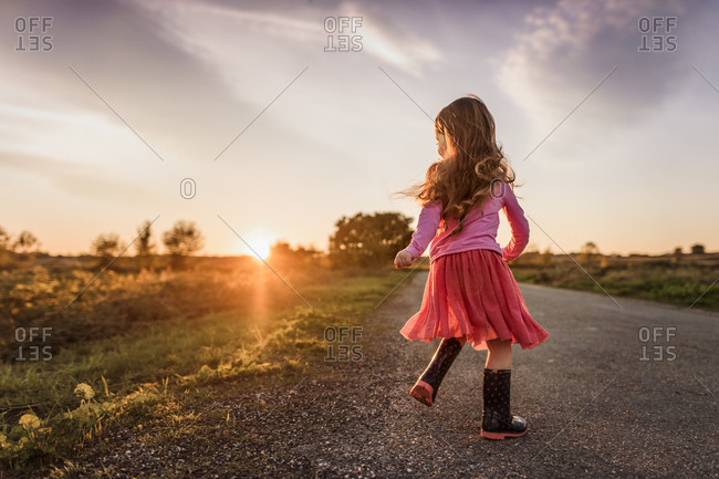 Girl plays in evening sun twirling on road with backlight