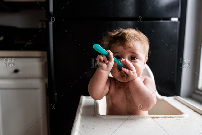 Close up of messy baby in high chair eating with spoon