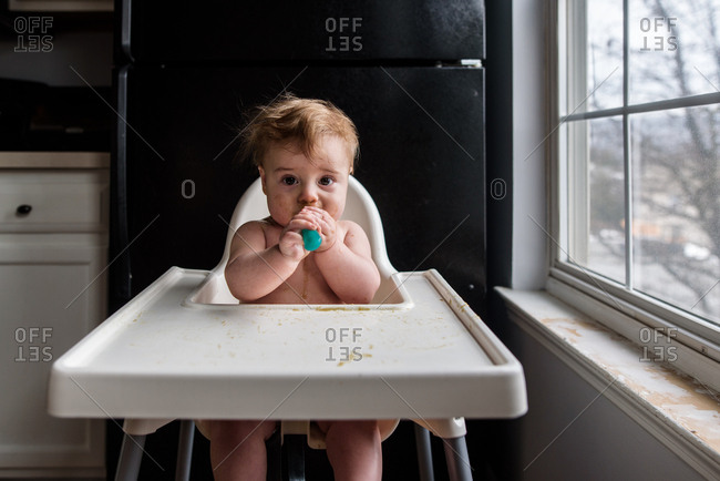 Messy baby in highchair eating with spoon