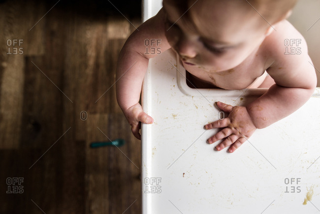 Overhead shot of messy baby's hands in highchair with spoon on floor