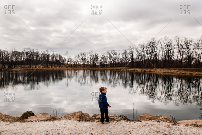 Wide shot of boy standing on edge of lake in winter time