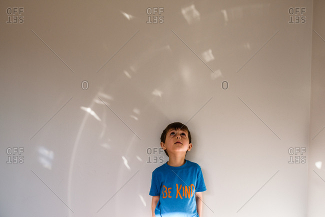 Boy wearing 'be kind' shirt looking up at light pattern on wall