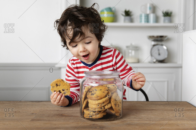 Cute toddler holding a cookie while looking into cookie jar