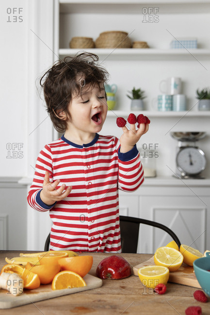 Funny child playing with fruits with raspberries on fingers